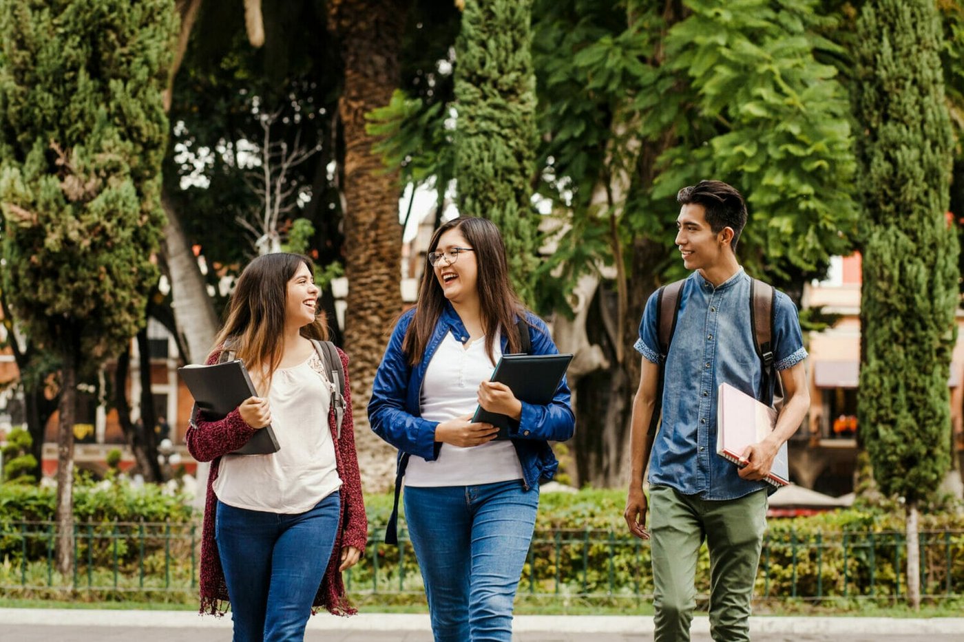 A group of three young Latinx students walking outdoors in a park in Mexico with their books.