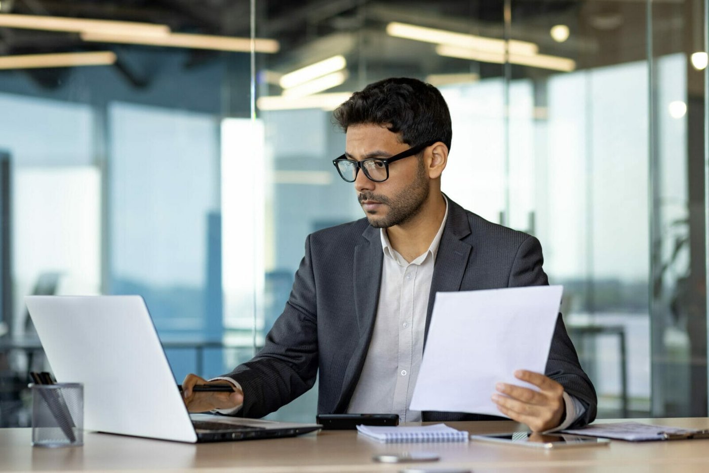 Serious concentrated hispanic businessman financier on paperwork inside office, man in business suit at workplace reviewing and reading papers, contracts and accounts reports. H-1B employer creates a public access file.